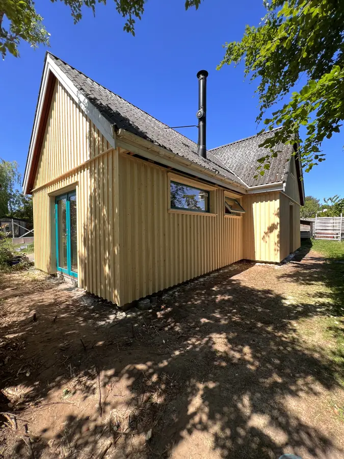 Hus med lys, lodret træbeklædning og turkise vinduer set fra haven