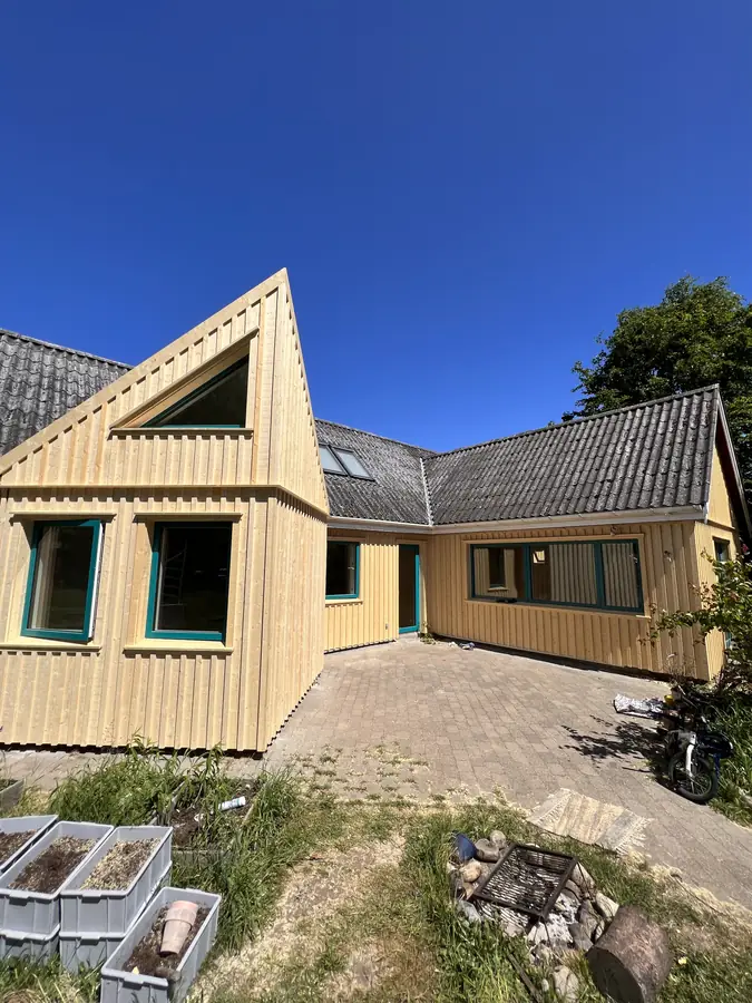 Hus med lodret træbeklædning, grønne vinduesrammer og ny gavl mod blå himmel