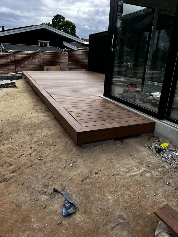 Terrasse i hårdttræ under opbygning ved sort hus